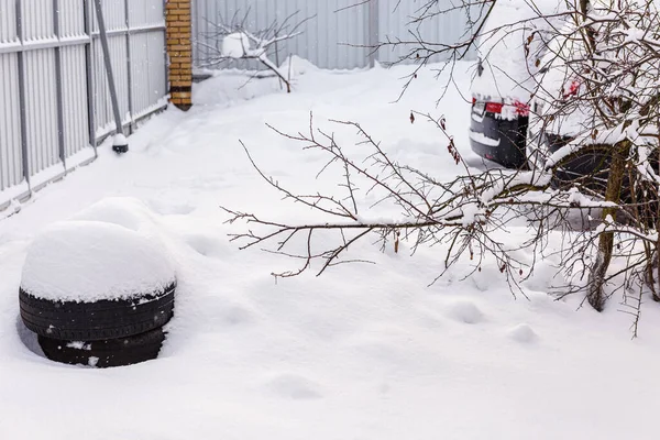 白い雪の上に車のタイヤ 雪に覆われた車のタイヤ 雪の接近の雪のドリフトで夏のタイヤ 夏用タイヤを冬用に交換する時期です 車のタイヤは家の中庭に横たわっている — ストック写真