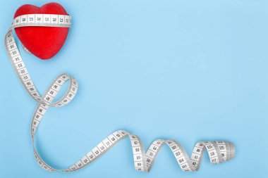 Kırmızı kalp mavi arka planda, esnek bir cetvelle sarılıp kopyalanıyor. Sağlıklı yaşam tarzı kavramı. Fitness için esnek çizgi.