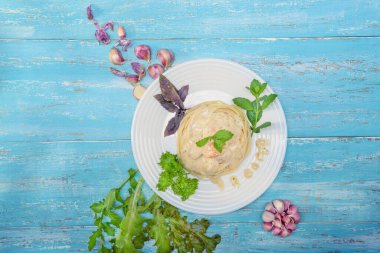 Mavi ahşap bir masada İtalyan makarnası ve sebze ve sarımsakla süslenmiş Provencal otlarla dolu bir tavukla dolu bir tabak var..