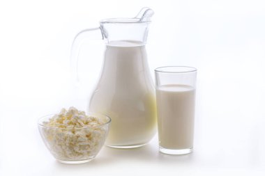 Bardaktaki lezzetli süt ve beyaz arka planda bir kase süzme peynirli sürahi. Sabah kahvaltısı için süt ürünleri çok sağlıklıdır..