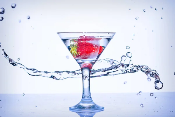 Frozen explosion of freshness from water, in a cocktail glass with strawberries, on a white background.