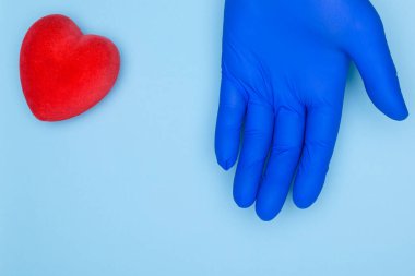 Mavi eldivenli doktor ve mavi arkaplanda kırmızı kalp. Kardiyoloji ve kalp hastalığı konsepti. Sağlık sigortası veya aşk konsepti..