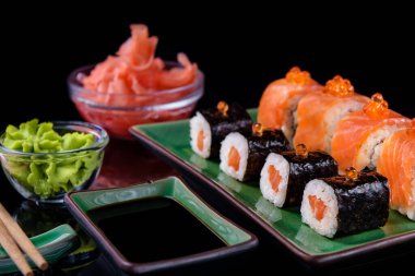 Japon yemeği. Bir dizi somon, yılan balığı, karides ve kırmızı havyar, güzel yeşil bir kasede, siyah bir arka planda yansıması olan..