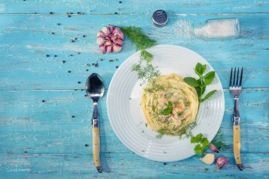 Tabak mavi ahşap bir masanın üzerinde duruyor, İtalyan makarnası ve tavuk Provencal otlarla süslenmiş, tuz ve sarımsakla süslenmiş.
