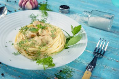 Tabak mavi ahşap bir masada duruyor, İtalyan makarnası ve sebze soslu tavuk, yeşil, tuz ve sarımsak ile süslenmiş, yakın plan..