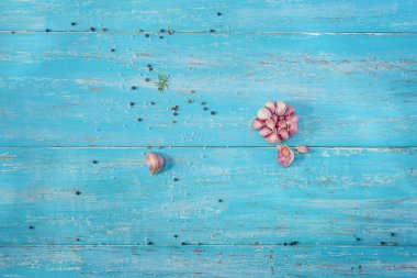 Sarımsak ve baharatların saçıldığı turkuaz ahşap bir masa.