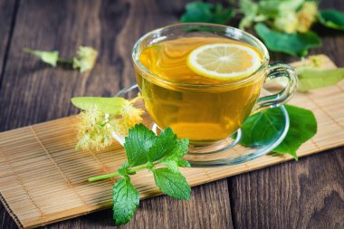 Yeşil çay. Çayı iyileştiriyorum. Çerçevelerden çay. Bir fincan şifalı kireç çayı, ahşap bir masanın üzerinde, kokulu ıhlamur çiçekleriyle çevrili, gün ışığı ışınlarıyla.