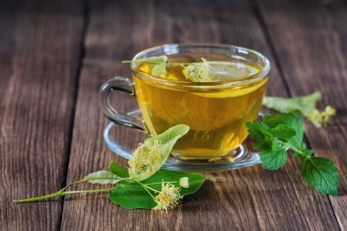 Yeşil çay. Çayı iyileştiriyorum. Çerçevelerden çay. Bir fincan çay, ahşap bir masanın üzerinde, kokulu ıhlamur çiçekleriyle çevrili, gün ışığında..