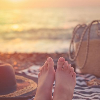 Mavi okyanus arka planda, güneş ışığında. Yaz bayramı için kadın plaj aksesuarları: hasır şapka, güneş gözlüğü, plaj çantası ve çizgili havlu, deniz kabuğu..