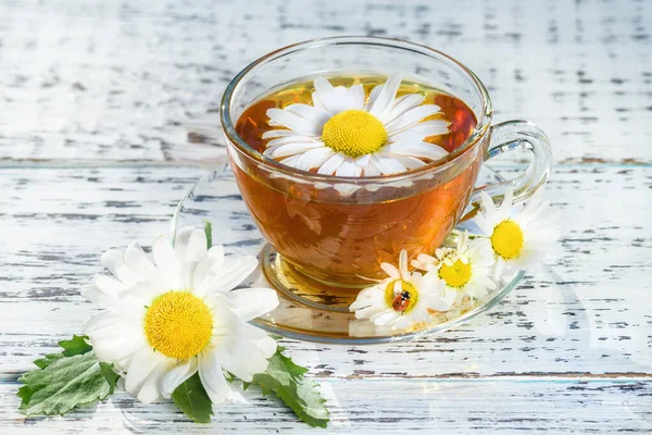 Cup of tea with chamomile, close-up, lit by sunlight, on a white wooden table. Cup of green tea with chamomile. Chamomile tea.