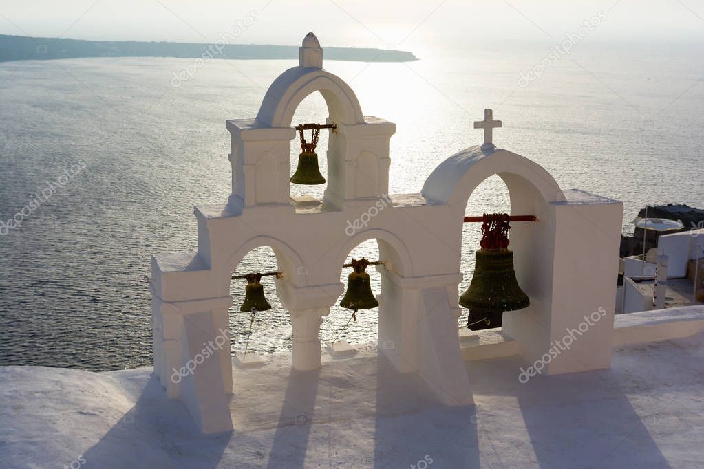 Arch with cross and bells of traditional Greek white church in Oia village, Santorini Island, Greece.