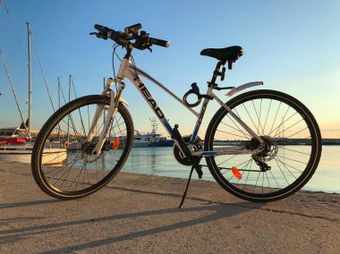 BURGAS, BULGARIA - 11 Ekim 2020: deniz kenarına park edilmiş Head şirketinin mavi ve beyaz bisikleti. Bulgaristan 'ın Burgaz kenti yakınlarındaki Sarafovo balıkçılık limanı gün batımında.