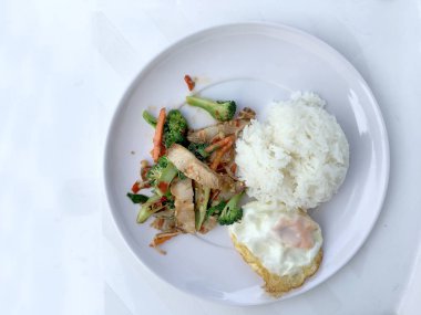 Kavrulmuş Chili Yapıştır ve karışık sebze soslu kızarmış gevrek domuz eti ilave edin; fesleğen; Kale; brokoli; havuç; kırmızı biber ve sahanda yumurta beyaz arka plan üzerinde beyaz tabak içinde Tayland Yasemin pirinç ile. Tay tarzında gıda.