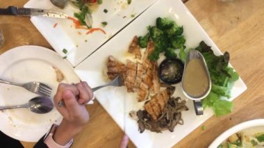 Bıçak ve çatalla ızgara bifteği yemek setiyle birlikte beyaz tabakta kesen bir kadın ve restorandaki ahşap masada bitiren bir kadın. Üst görüntü görüntüleri.