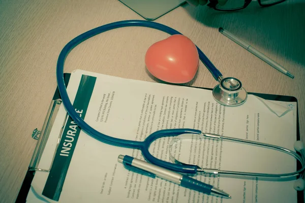 Workplace of doctor with laptop, stethoscope, small red heart  and glasses notebook on wooden table in the office.   Blood Pressure Monitor. Medical equipment. Cardiac diagnosis. vintage tone.