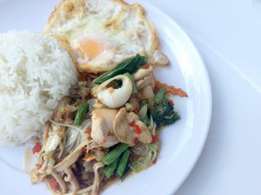 Kızarmış baharatlı deniz ürünleri fesleğen yaprakları ve karışık sebze ve pirinç yasemin beyaz tabak kızarmış yumurta ile kızarmış. Tay tarzında gıda.