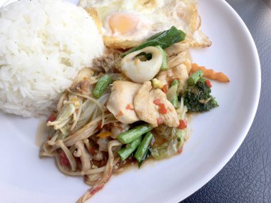 Kızarmış baharatlı deniz ürünleri fesleğen yaprakları ve karışık sebze ve pirinç yasemin beyaz tabak kızarmış yumurta ile kızarmış. Tay tarzında gıda.