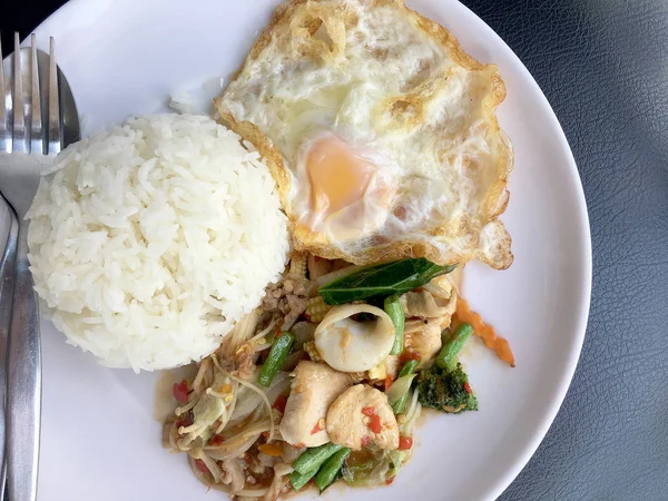 Kızarmış baharatlı deniz ürünleri fesleğen yaprakları ve karışık sebze ve pirinç yasemin beyaz tabak kızarmış yumurta ile kızarmış. Tay tarzında gıda.