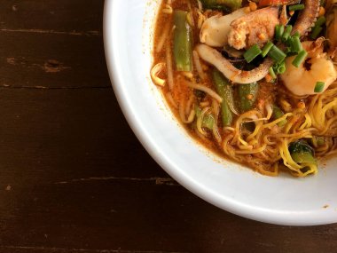 Karides, kalamar ve kabuklu deniz ürünleri ahşap masa, Tom Yum Goong üzerinde beyaz kase lezzetli Asya baharatlı deniz ürünleri şehriye çorbası. Tay tarzı yiyecek. Vintage tonu renk filtresi.