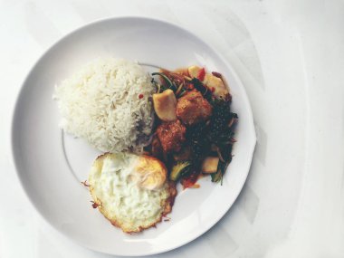 Baharatlı karıştırın kızarmış balık fileto pirinç ve beyaz arka plan üzerinde beyaz tabak kızarmış yumurta ile Tay ot ile. Vintage rengi.