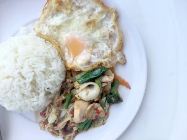 Kızarmış baharatlı deniz ürünleri fesleğen yaprakları ve karışık sebze ve pirinç yasemin beyaz tabak kızarmış yumurta ile kızarmış. Tay tarzında gıda.