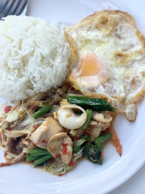 Kızarmış baharatlı deniz ürünleri fesleğen yaprakları ve karışık sebze ve pirinç yasemin beyaz tabak kızarmış yumurta ile kızarmış. Tay tarzında gıda.