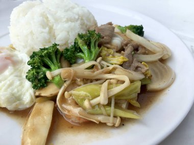 Tayland mutfağı. Tavada kızartılmış renkli sebze, soğan, brokoli, mantar etli pilav ve kızarmış yumurta beyaz arka plan üzerinde beyaz tabak içinde. Hızlı sokak restoran Tay tarzında gıda.