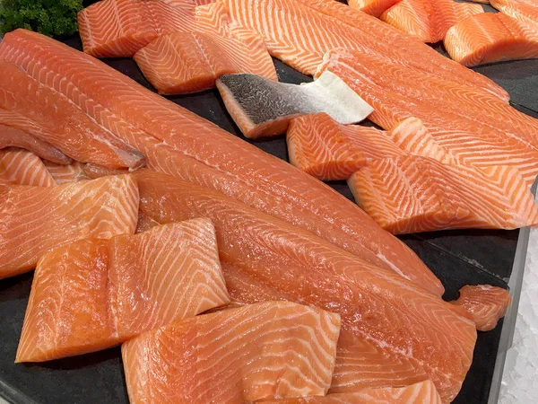 Sliced raw salmon or fresh salmon. Salmon fillets for sale at market displayed with a patchwork effect. Many fresh salmon fish meat slices in a black tray which are sale in the supermarket.