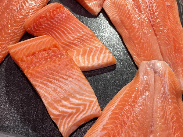 Sliced raw salmon or fresh salmon. Salmon fillets for sale at market displayed with a patchwork effect. Many fresh salmon fish meat slices in a black tray which are sale in the supermarket.