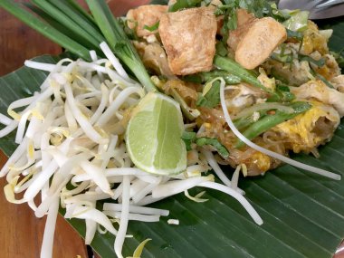 Pad Thai. Ahşap masada muz yaprağı üzerinde karides karides ve sebze ile Tay tarzı kızarmış erişte. Restoran için geleneksel Tay yemek menüsü. Asya yemekleri. Üst tenli ve düz lay