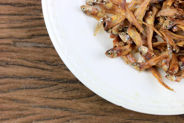 Fried giant catfish and pile of Deep fried small fishes (Minnow fish) Traditional Thai recipes in white dish on rustic wood background.  popular in Thailand, important export product of Thailand.