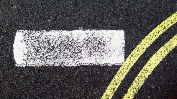 Close-up on road markings: a white line and two curved and parallel yellow lines painted on the asphalt of a street in London, England, UK. Rough texture. Patina, colors and natural light.