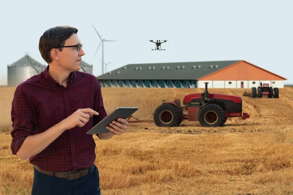 Farmer with digital tablet controls an autonomous tractor and drone on a smart farm