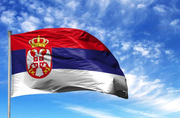 National flag of Serbia on a flagpole in front of blue sky
