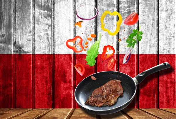 Cooking process. Hot movement. Fresh vegetables falling into the pan with meat, cooking concept on wooden flag background of Poland