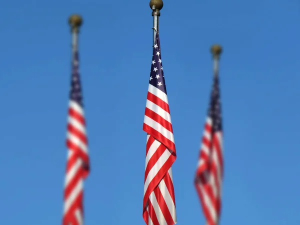 National flag of America on a flagpole in front of blue sky.