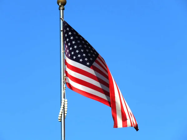 National flag of America on a flagpole in front of blue sky.