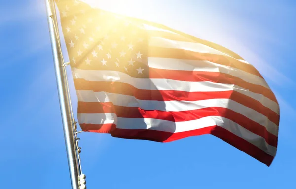 National flag of America on a flagpole in front of blue sky.