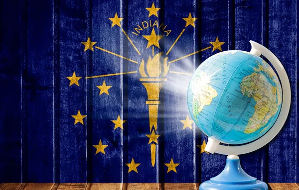 Globe with a world map on a wooden background with the image of the flag State of Indiana. The concept of travel and leisure abroad.