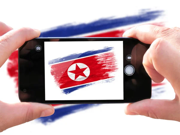 brush painted flag of North Korea. The hands of men make a photo from the phone. Shooting from the smartphone.