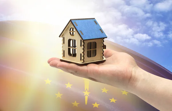 The concept of real estate mortgages, citizenship and accommodation. In hands holding a model of a wooden house against the background of the flag of State of Indiana.