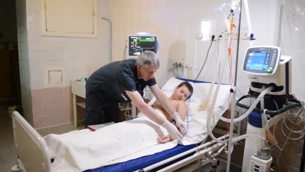 Menino deitado na cama do hospital e sorrindo enquanto ouve o médico masculino escrevendo na área de transferência — Vídeo de Stock
