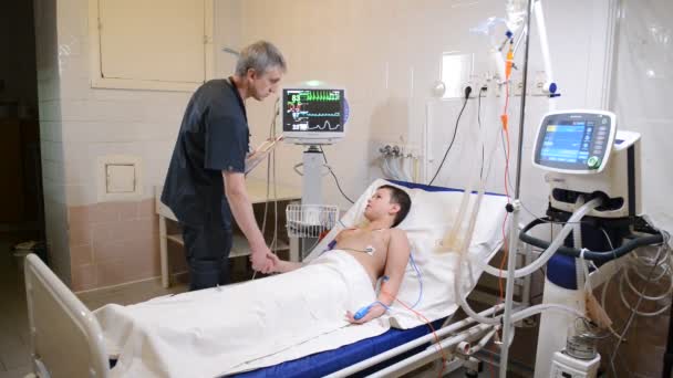 Kleine jongen liggend op ziekenhuisbed en glimlachen terwijl u luistert naar mannelijke arts schrijven op Klembord — Stockvideo