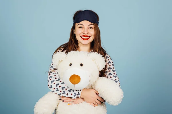 En vacker ung kvinna klädd i pyjamas kramar hennes uppstoppad nallebjörn — Stockfoto