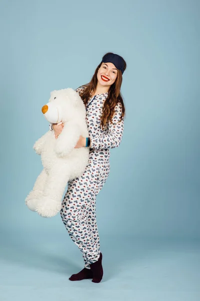 En vacker ung kvinna klädd i pyjamas kramar hennes uppstoppad nallebjörn — Stockfoto