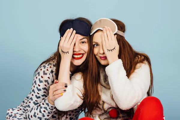 Två skrattande flickvänner i pyjamas och med en sömn mask blunda för varandra — Stockfoto