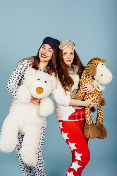 Two happy girls in pajamas hold toys in their hands — Stock Photo, Image