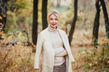 Güzel sarışın kadın sonbahar parkında vakit geçiriyor.