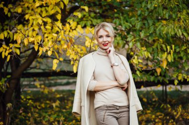 Güzel sarışın kadın sonbahar parkında vakit geçiriyor.