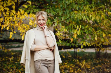 Güzel sarışın kadın sonbahar parkında vakit geçiriyor.